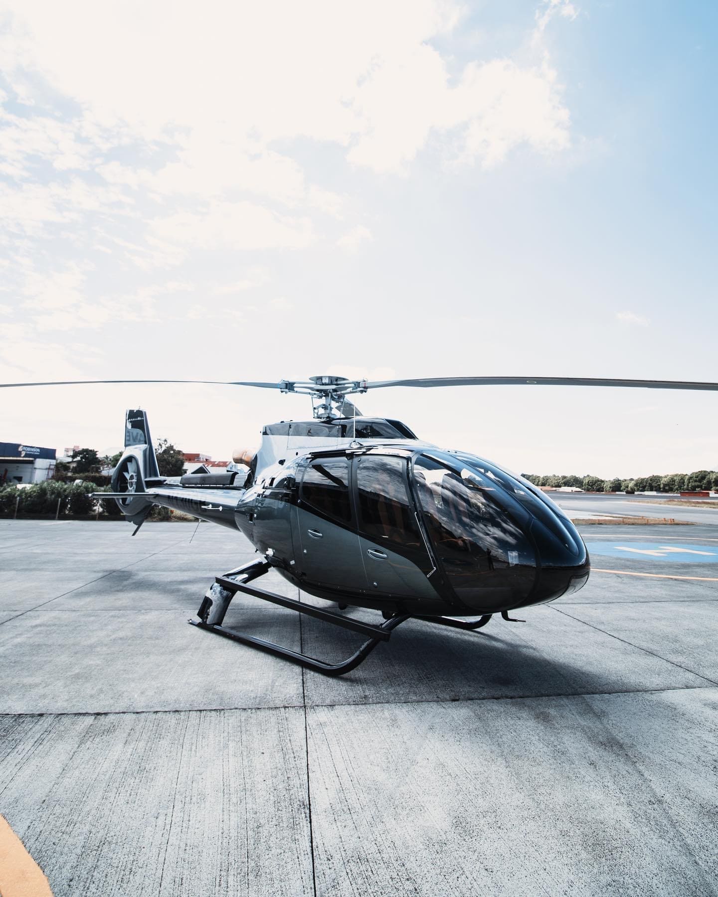 Black EC130 helicopter parked on the apron at La Aurora airport, Guatemala, rotor blades against an open sky